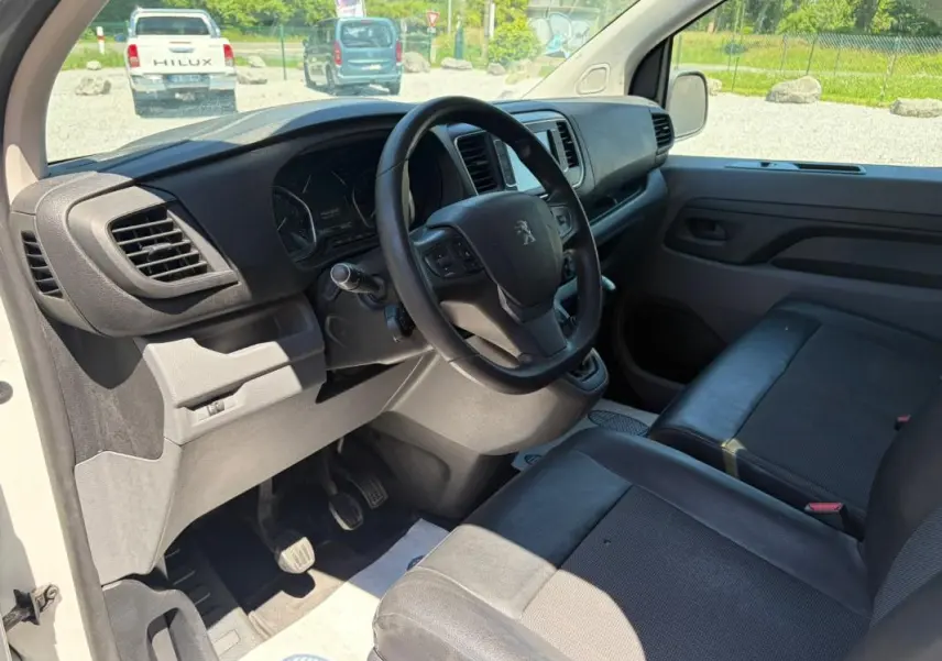 Vue intérieure côté conducteur du Peugeot Expert Fourgon blanc 2019, volant cuir multifonctions et sièges en tissu noir.