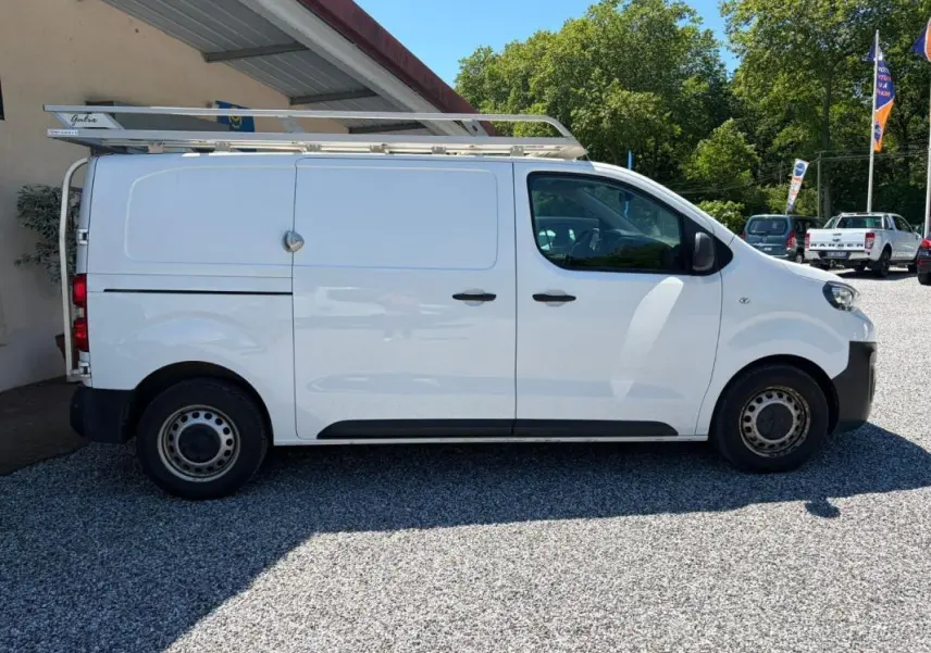 Peugeot Expert Fourgon blanc en vue de profil côté gauche, avec galerie de toit et portes coulissantes fermées.