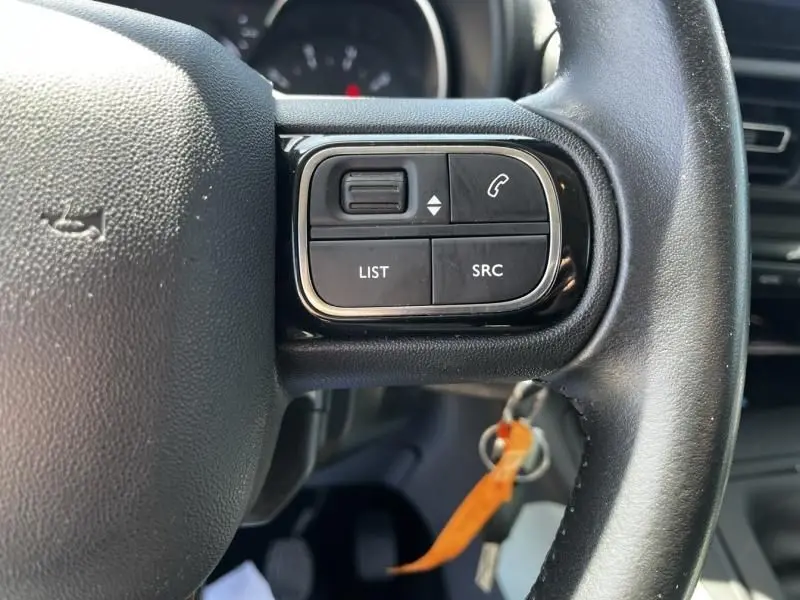Gros plan sur les commandes au volant côté gauche du Citroën Berlingo XL gris métal, version 2021, avec boutons de gestion audio et appel.