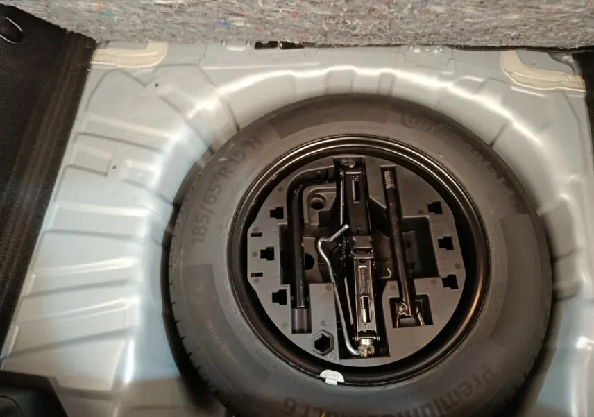 Vue plongeante sur la roue de secours et les outils de bord dans le coffre d'une Renault Clio gris clair.