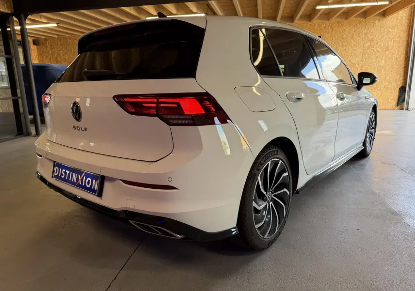 Volkswagen Golf 2.0 TDI 150 DSG7 R-Line blanc vue 3/4 arrière droit en intérieur avec jantes noires et feux allumés.