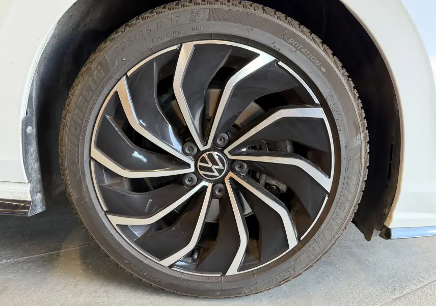 Gros plan sur la roue avant gauche d'une Volkswagen Golf blanche 2023 avec jante alliage noire et argentée R-Line.