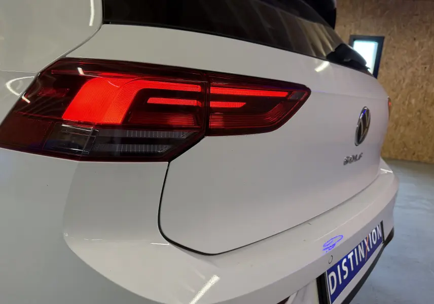 Vue arrière droite d'une Volkswagen Golf blanche 2.0 TDI 150 DSG7 R-Line avec feux arrière allumés en intérieur.