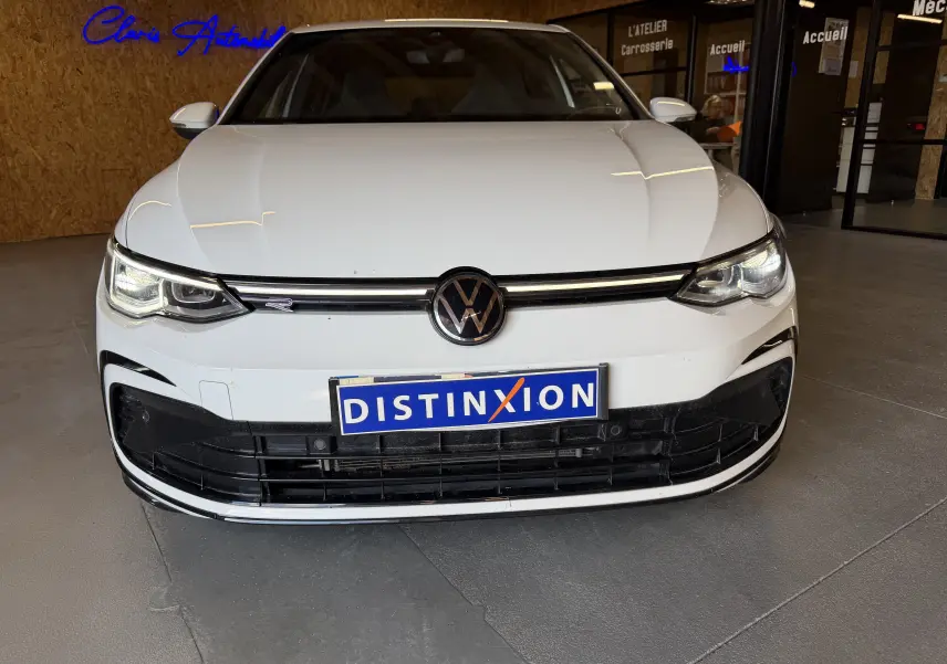 Vue de face d'une Volkswagen Golf 2.0 TDI 150 DSG7 R-Line blanche, avec phares allumés et calandre noire distinctive.