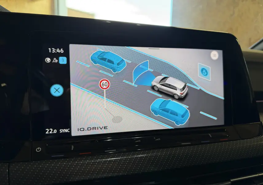 Écran intérieur montrant l'aide au stationnement avec une Volkswagen Golf blanche en vue de dessus, entourée de voitures bleues.
