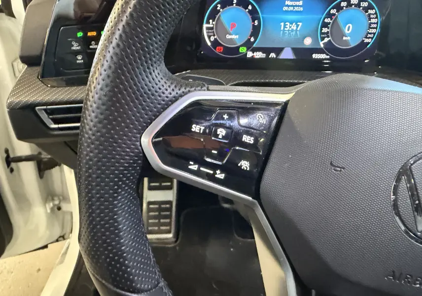 Gros plan sur le volant et le tableau de bord numérique d’une Volkswagen Golf blanche 2.0 TDI 150 DSG7 R-Line, avec commandes au volant visibles.
