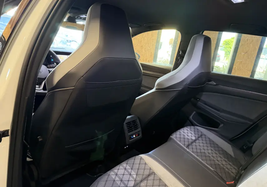 Vue intérieure arrière droite de la Volkswagen Golf 2.0 TDI R-Line 2023 blanche, montrant les sièges avant en cuir noir et tissu gris à motifs.