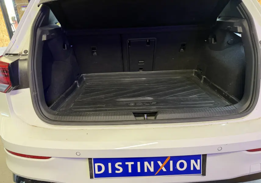 Coffre ouvert d'une Volkswagen Golf blanche 2023, vue arrière, avec tapis de coffre marqué "Golf" visible.