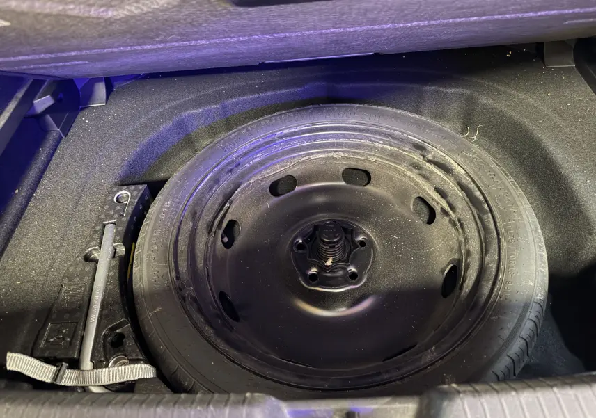 Vue rapprochée de la roue de secours noire dans le coffre d'une Volkswagen Golf 2.0 TDI 150 DSG7 R-Line blanche.