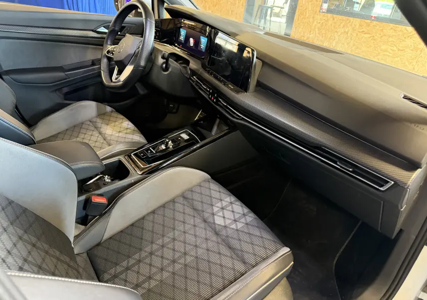 Vue intérieure côté conducteur de la Volkswagen Golf 2.0 TDI 150 DSG7 R-Line 2023 avec sièges tissu à motif et tableau de bord moderne noir.