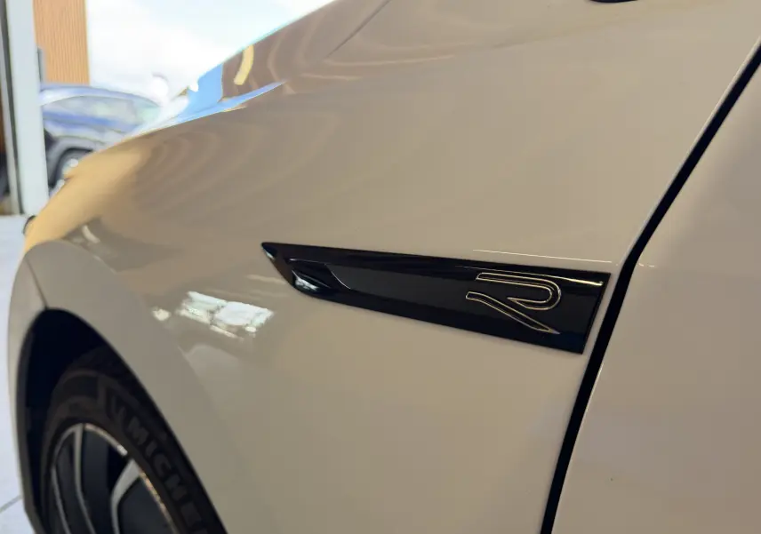 Gros plan sur l'aile avant gauche blanche d'une Volkswagen Golf 2.0 TDI R-Line avec logo "R" noir distinctif.