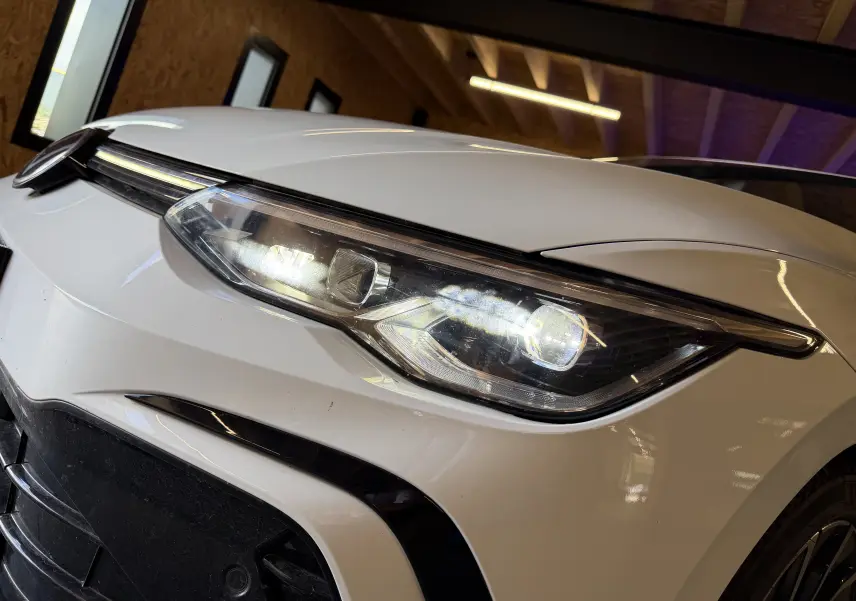 Gros plan sur le phare avant droit allumé d'une Volkswagen Golf 2.0 TDI blanche, version R-Line 2023.
