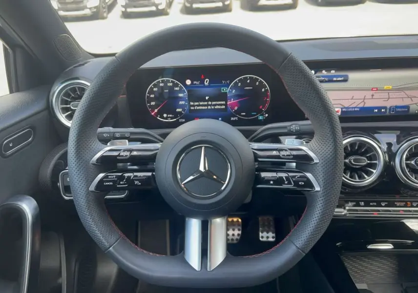 Vue intérieure centrée sur le volant cuir perforé AMG de la Mercedes Classe A 200 7G-DCT avec tableau de bord digital et aérateurs ronds.
