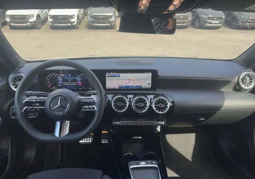 Vue intérieure avant de la Mercedes Classe A 200 AMG Line 2025, tableau de bord noir avec écran digital et aérateurs ronds chromés.
