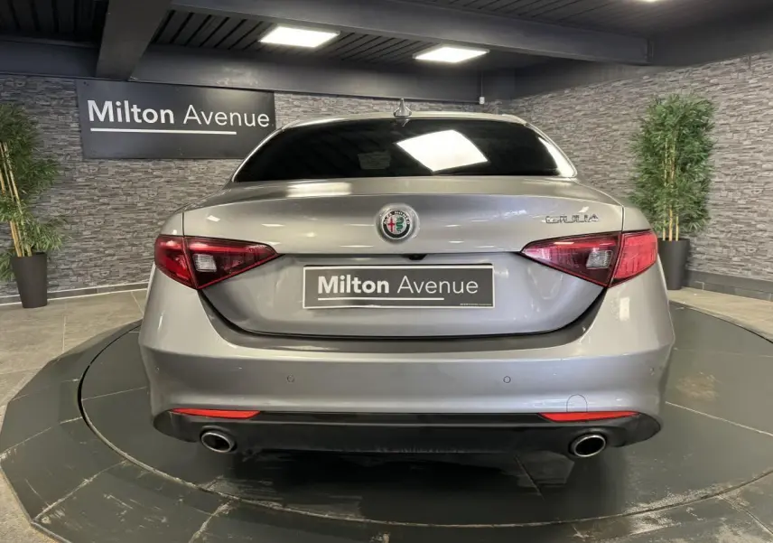 Vue arrière d'une Alfa Romeo Giulia gris métallisé avec feux LED et double sortie d'échappement dans un showroom.