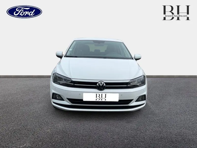 Vue frontale d'une Volkswagen Polo blanche Pure avec calandre noire et phares halogènes allumés.