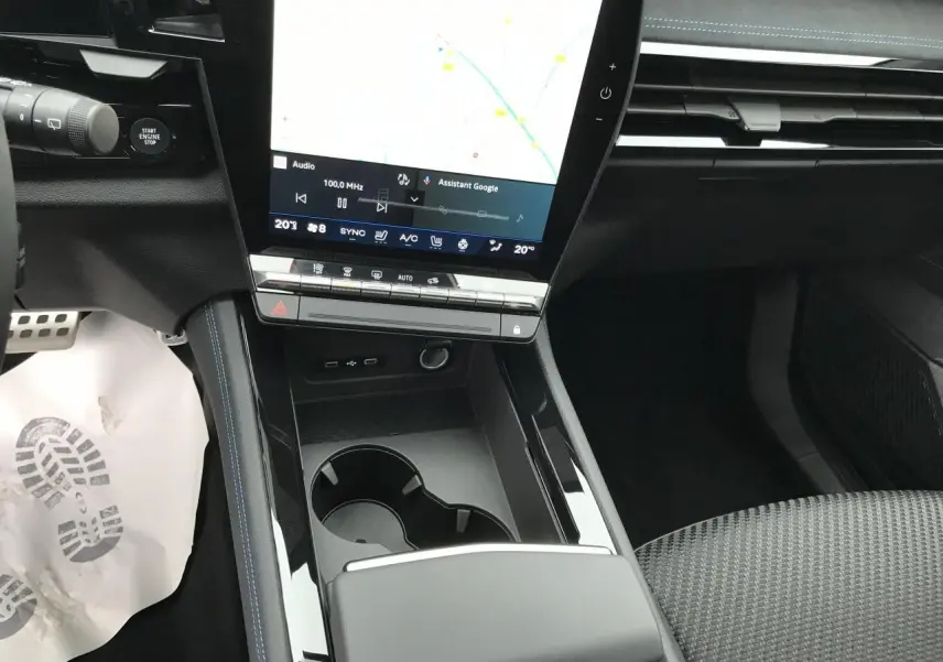 Vue intérieure centrée sur la console centrale noire brillante avec écran tactile vertical et sièges tissu gris.