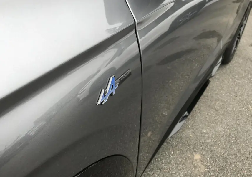 Gros plan sur l'aile avant gauche gris métallisé du Renault Austral avec badge Esprit Alpine bleu et noir.