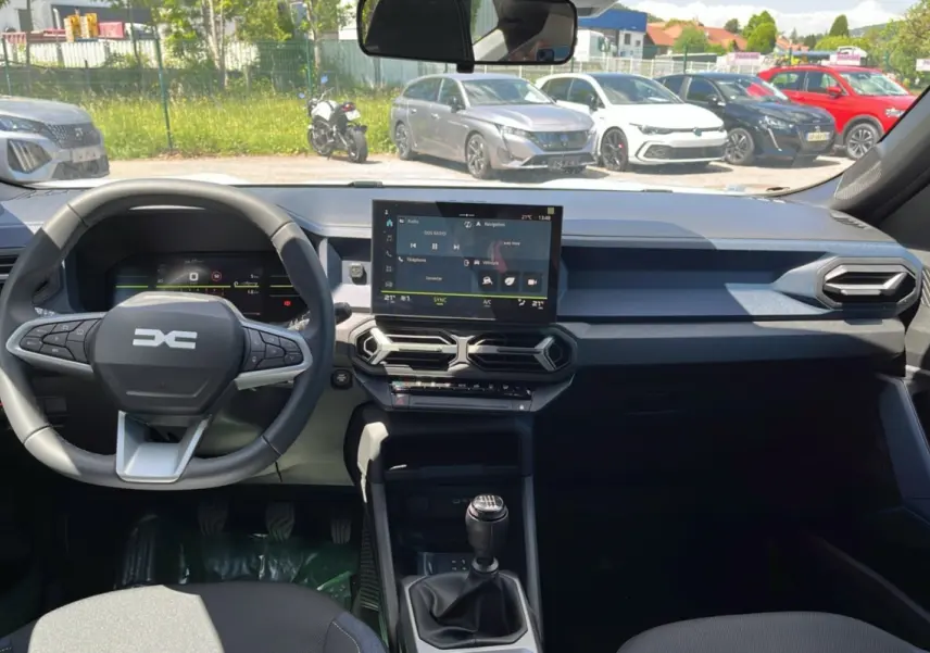 Vue intérieure avant du tableau de bord et volant cuir du Dacia Bigster blanc glacier avec écran tactile et boîte manuelle.