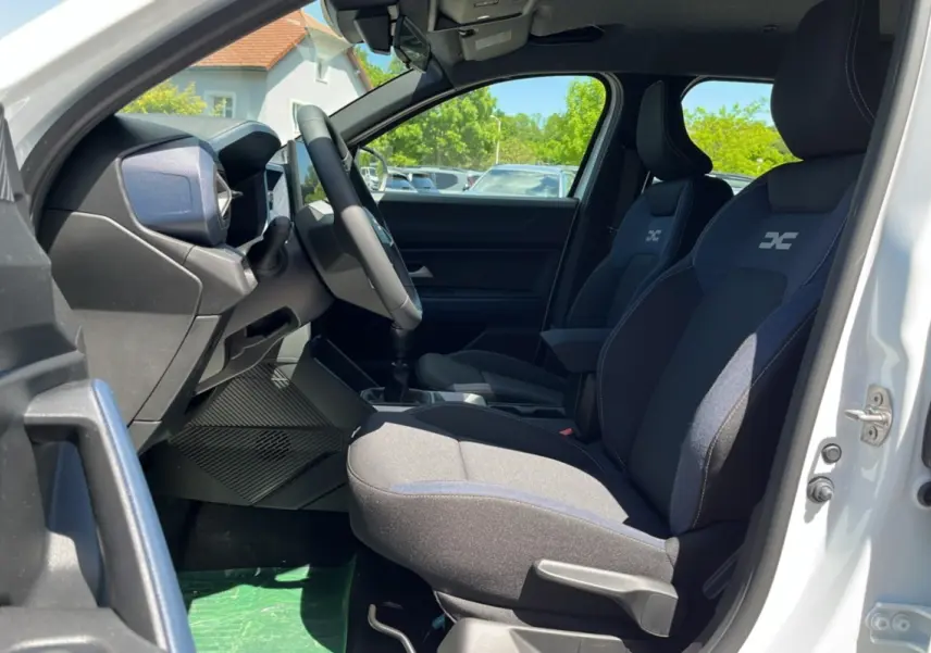 Intérieur côté conducteur du Dacia Bigster blanc glacier 2025, sièges tissu avec logo, volant cuir et levier de vitesses manuel.