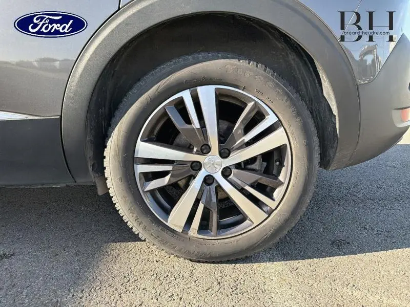 Gros plan sur la roue arrière droite d'un Peugeot 5008 gris Platinium avec jante alu à plusieurs branches.