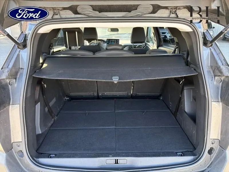 Vue arrière du coffre ouvert d'un Peugeot 5008 gris Platinium, avec banquette arrière et tablette cache-bagages visibles.
