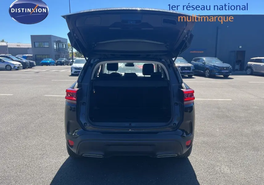 Vue arrière d'un Citroën C5 Aircross noir métal 2025 avec coffre ouvert sur parking extérieur ensoleillé.