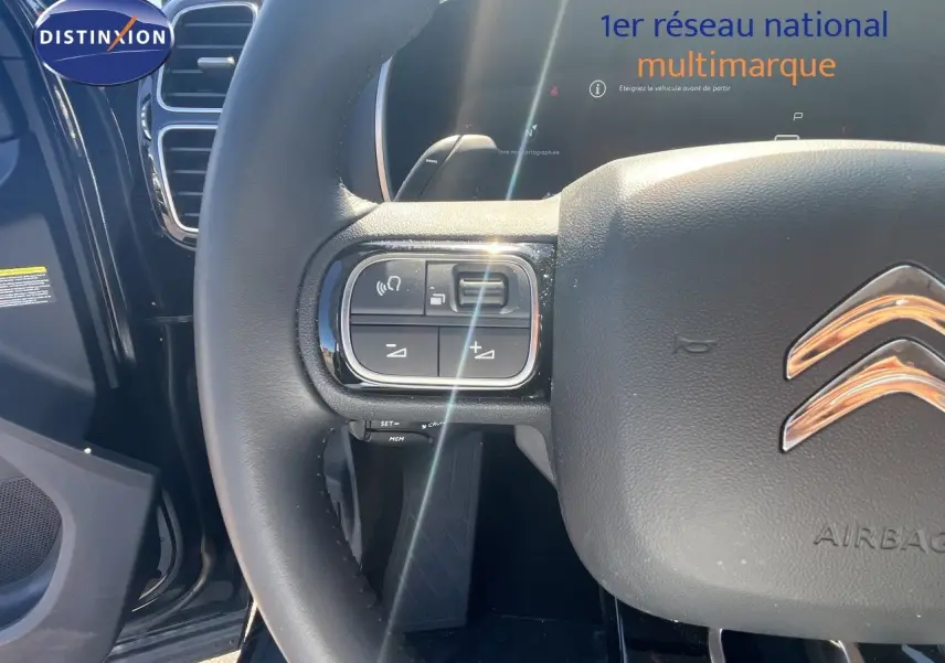 Gros plan sur le volant noir cuir du Citroën C5 Aircross 2025, avec commandes intégrées et logo chrome visible.