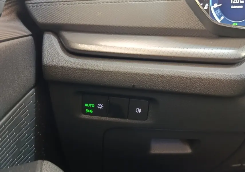 Détail intérieur côté gauche du tableau de bord noir avec commandes d’éclairage automatiques et antibrouillard allumées.