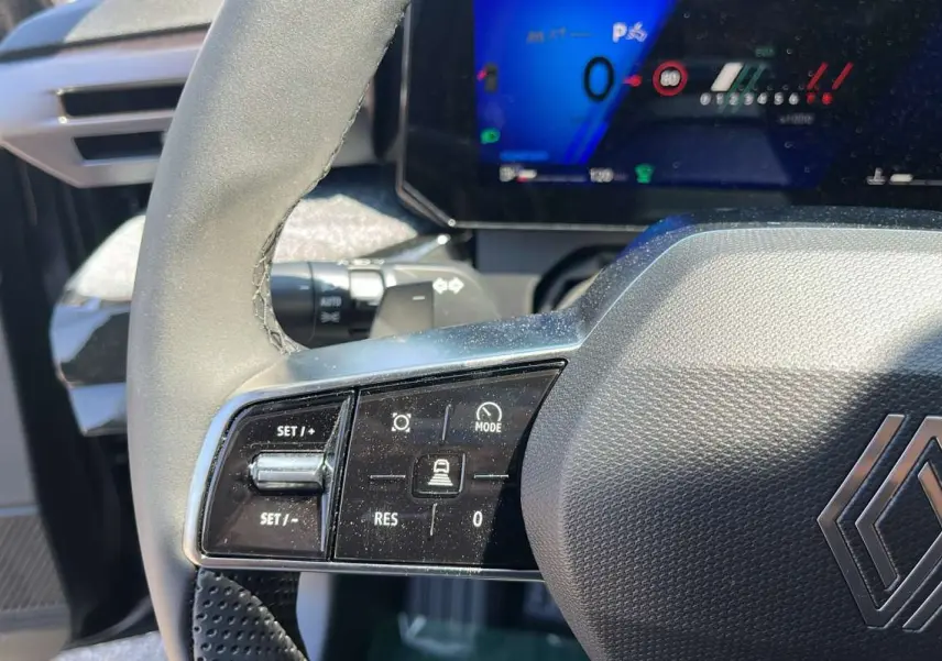 Gros plan sur le volant noir texturé de la Renault Clio 6 TCE 115 EDC TECHNO PLUS avec commandes multifonctions et tableau de bord digital.