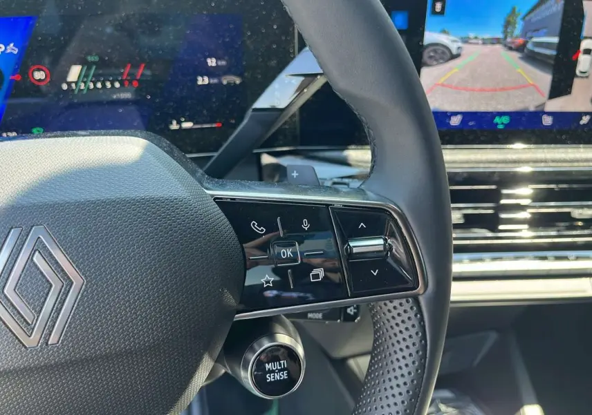 Gros plan sur le volant textile grainé noir étoilé de la Renault Clio 6 TCE 115 EDC avec commandes multifonctions et écran tactile.