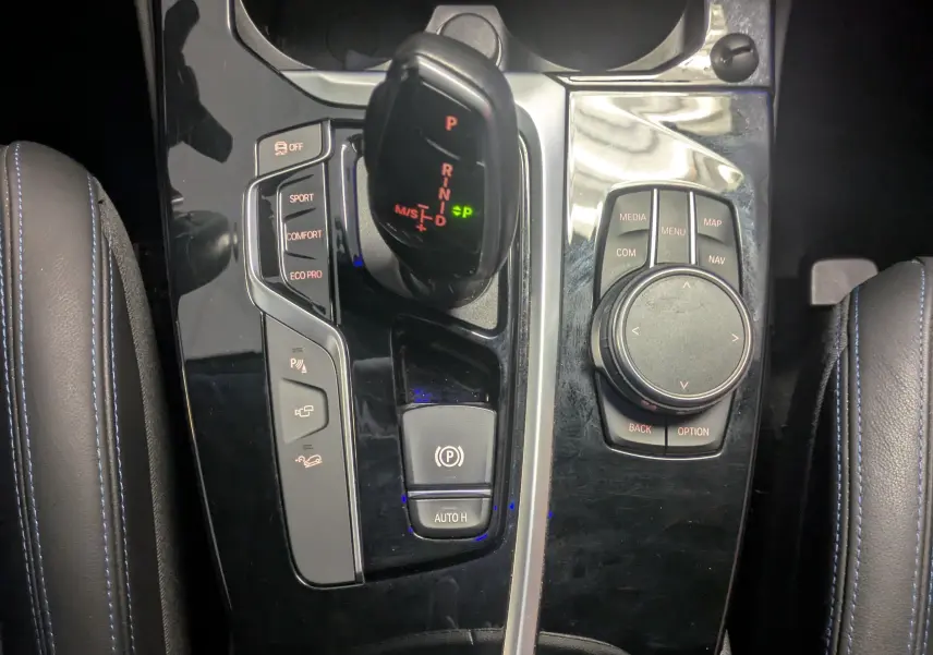 Vue rapprochée de la console centrale noire brillante du BMW X4 blanc 2021, avec levier de vitesses automatique et commandes multimédia.