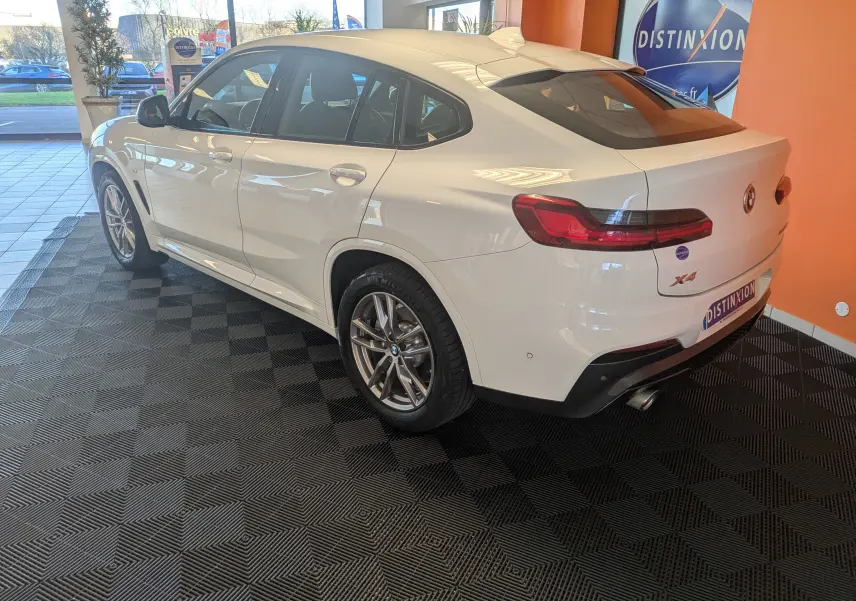 BMW X4 blanc en vue 3/4 arrière droit, soulignant ses lignes fluides et ses feux arrière LED distinctifs.