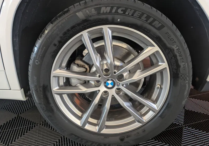 Gros plan sur la jante alliage argentée et pneu Michelin d'un BMW X4 blanc, mettant en valeur le logo BMW central.