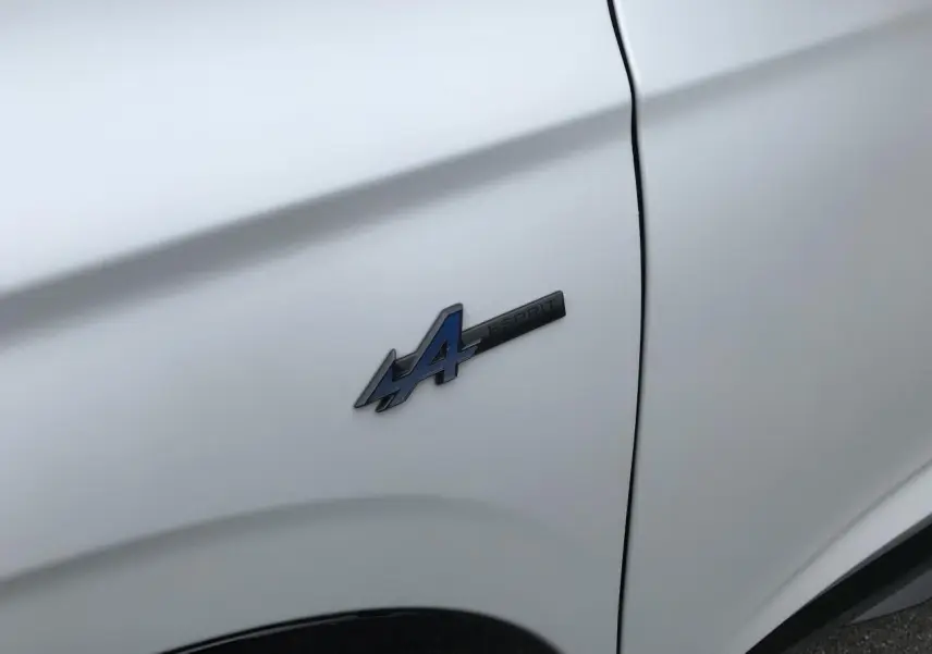 Gros plan sur l'écusson Esprit Alpine bleu sur l'aile avant gauche d'un Renault Austral blanc satin.