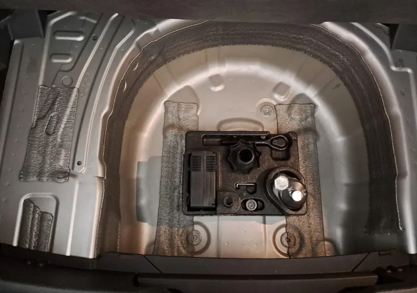 Vue plongeante sur le compartiment de roue de secours du Volkswagen T-Cross 2022 en reflet d'argent, avec outils de bord visibles.