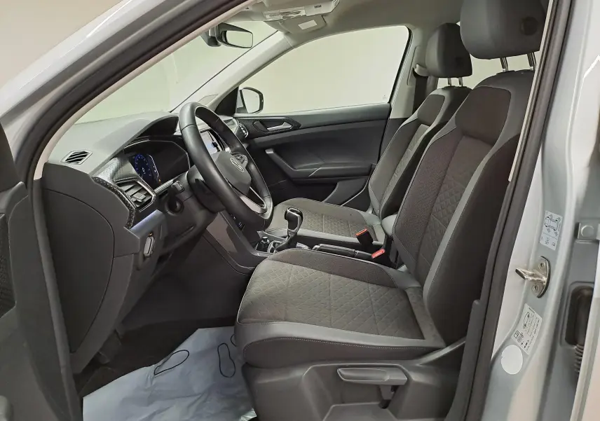 Vue intérieure côté conducteur du Volkswagen T-Cross 2022 argent, montrant sièges tissu gris et tableau de bord moderne.