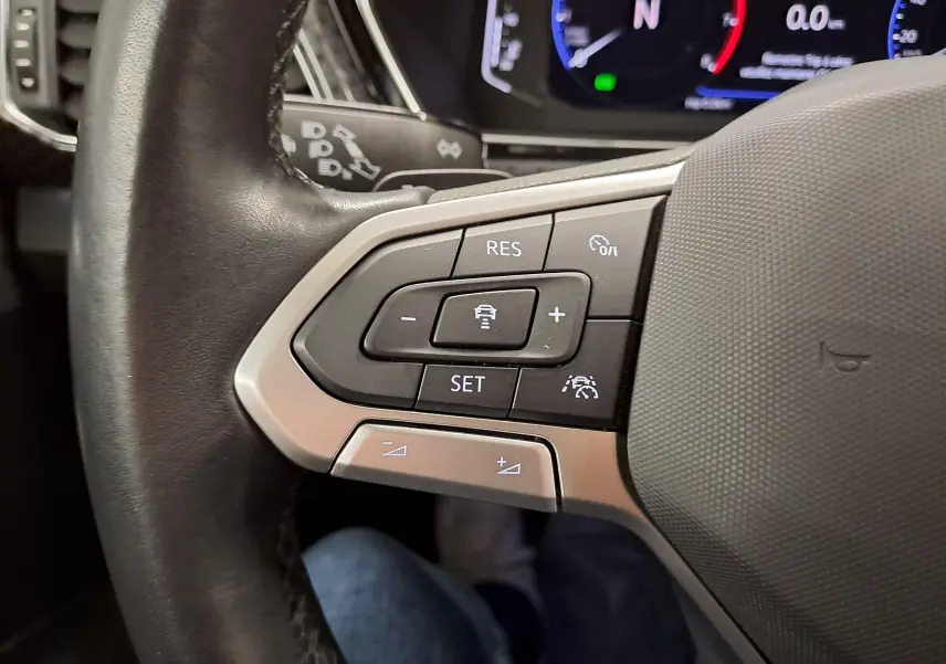 Gros plan sur les commandes au volant gauche du Volkswagen T-Cross 2022 R-Line, avec boutons de régulateur de vitesse et finition argentée.