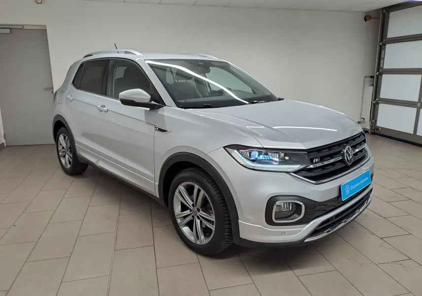 Volkswagen T-Cross 1.0 TSI R-Line 2022 en reflet d'argent, vue 3/4 avant droit avec phares allumés en intérieur.