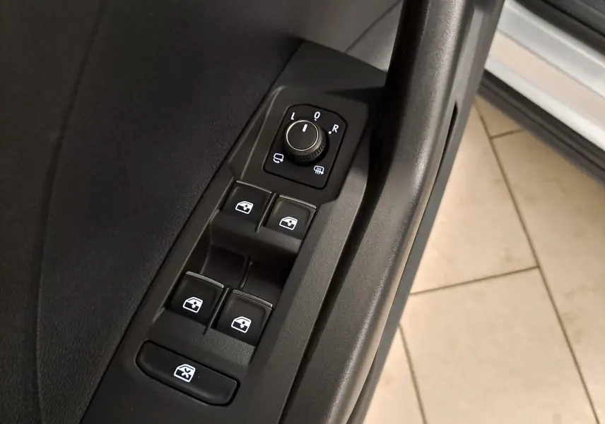 Gros plan sur les commandes de lève-vitres et réglage des rétroviseurs côté conducteur du Volkswagen T-Cross 2022 couleur reflet d'argent.