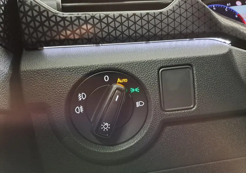 Détail du bouton de commande des phares avec éclairage automatique sur le tableau de bord noir du Volkswagen T-Cross 2022 reflet d'argent.