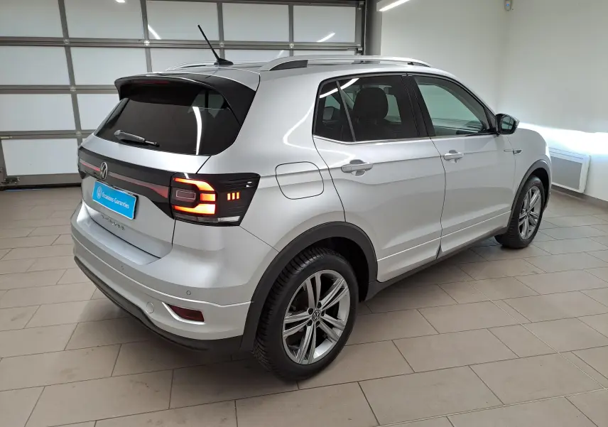 Vue 3/4 arrière droit d'un Volkswagen T-Cross 2022 argent reflet, version R-Line avec feux arrière allumés en intérieur.