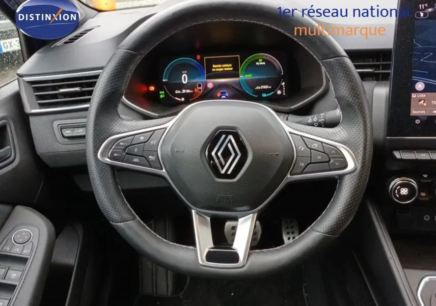 Vue intérieure centrée sur le volant noir perforé de la Renault Clio 1.6 E-TECH 2024 avec tableau de bord numérique et écran tactile.