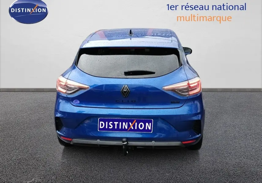 Vue arrière d'une Renault Clio 1.6 E-TECH hybride bleu Iron Metal avec attelage, sous une pluie légère.