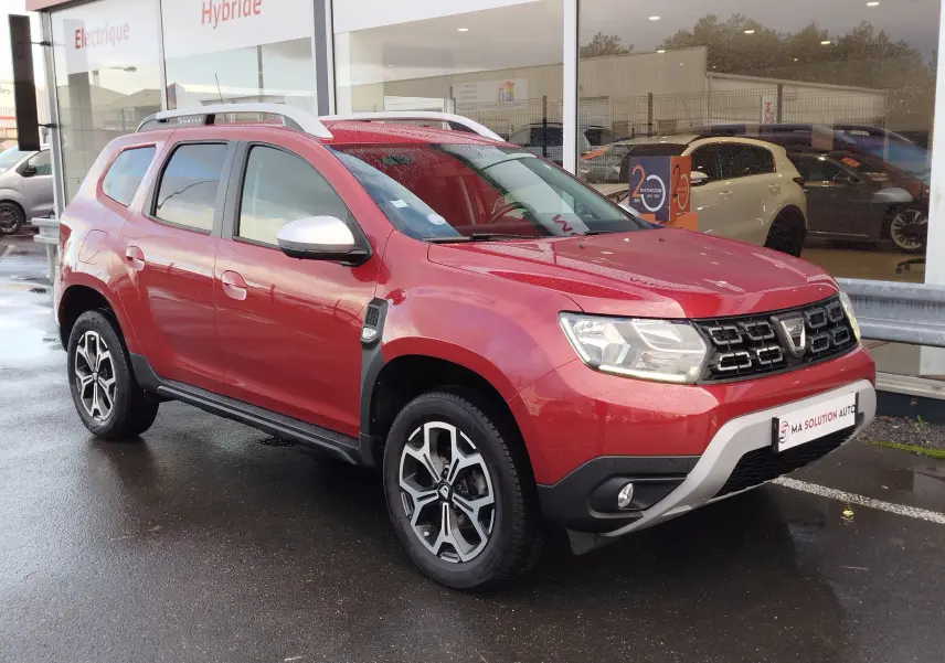 Vue 3/4 avant droit d'un Dacia Duster rouge Fusion 2020 avec jantes alliage bicolores et barres de toit argentées.