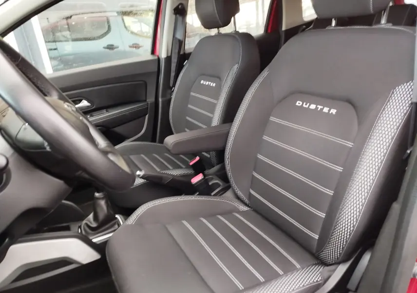 Vue intérieure côté conducteur du Dacia Duster 2020 rouge Fusion, mettant en valeur les sièges noirs avec logo Duster brodé.