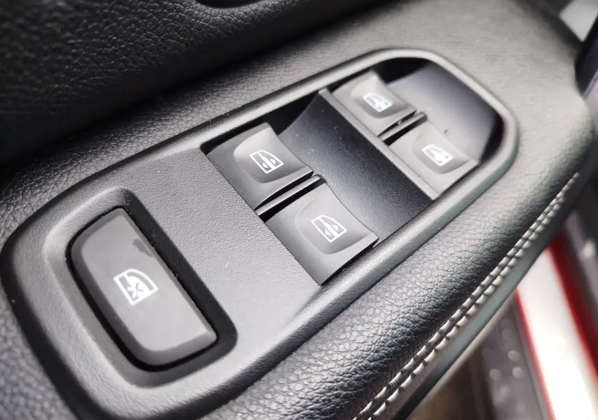 Gros plan sur les commandes des vitres électriques côté conducteur du Dacia Duster 2020, intérieur noir avec surpiqûres blanches.