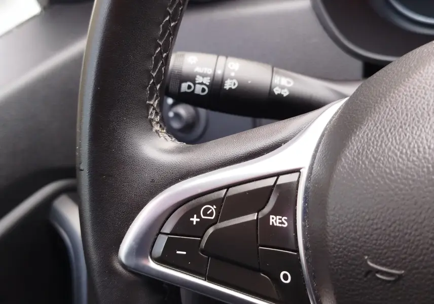 Gros plan sur les commandes au volant gauche du Dacia Duster 2020 rouge, avec boutons de régulateur de vitesse visibles.