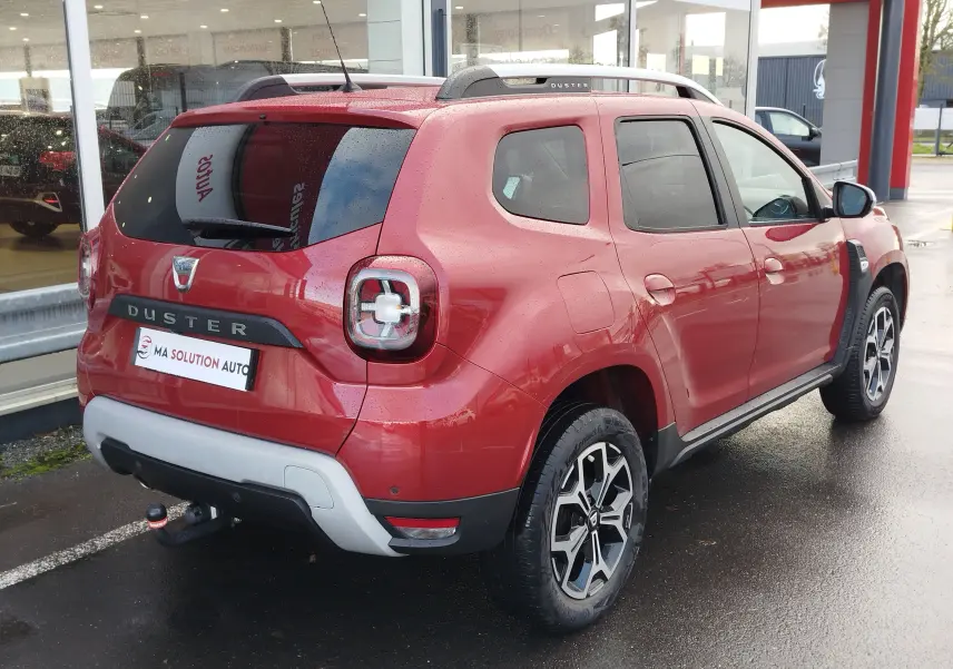 Vue 3/4 arrière droite du Dacia Duster rouge Fusion 2020 avec barres de toit et jantes bi-ton distinctives.