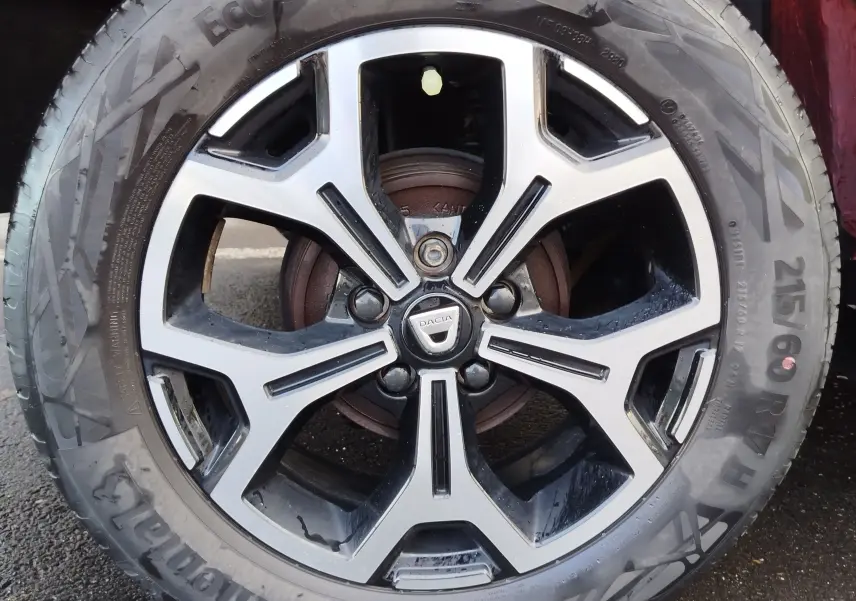 Gros plan sur la jante alliage bicolore du Dacia Duster rouge fusion, mettant en valeur le logo central et le pneu Continental.